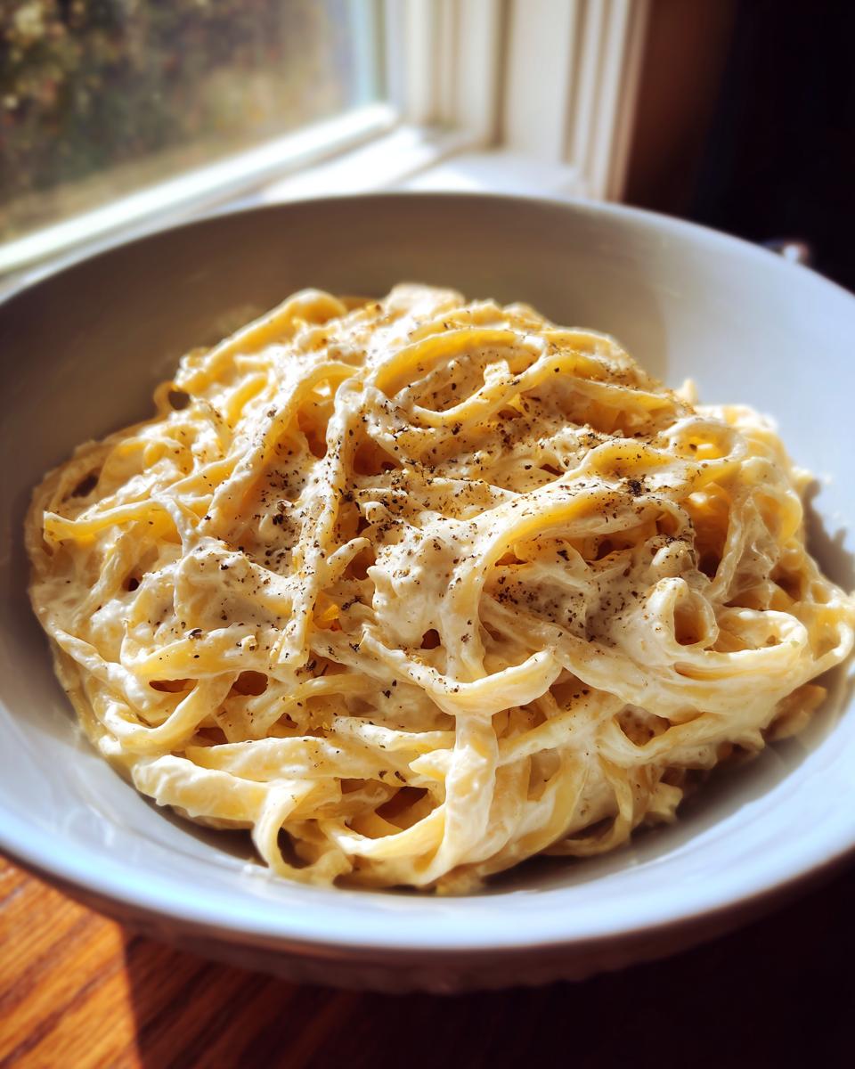 A close-up of fettuccine pasta coated in creamy vegan alfredo sauce and topped with cracked black pepper.