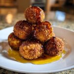 A stack of crispy, golden brown goat cheese balls drizzled with dark honey or syrup on a white plate.