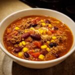 Close-up of a white bowl filled with rich, hearty crockpot cowboy soup featuring ground beef, kidney beans, corn, and tomatoes.