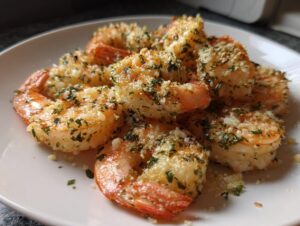 Close-up of several cooked air fryer shrimp coated in garlic, Parmesan, and parsley, served on a white plate.