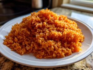A close-up mound of vibrant, orange-red jollof rice served on a simple white plate.