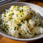 Close-up of fluffy cilantro lime rice topped with chopped green herbs and bright yellow lemon zest.
