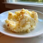A serving of fluffy garlic mashed potatoes topped with crispy browned bits, presented on a white plate.