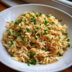 Close-up of a fluffy rice pilaf recipe served in a white bowl, topped with fresh chopped parsley.