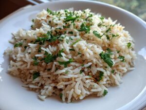 A close-up of a serving of fluffy rice pilaf recipe garnished generously with chopped fresh green parsley.