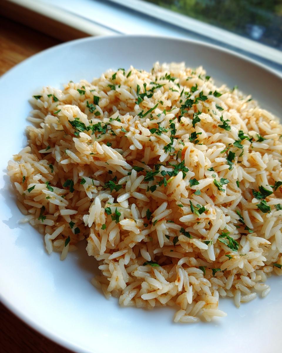 A close-up of fluffy, seasoned rice pilaf recipe garnished with fresh chopped parsley, served on a white plate.