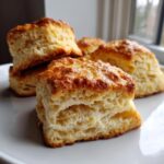 Close-up of several flaky, square scones stacked on a white plate, showing their layered interior.