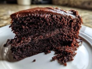 Close-up of a rich, dark slice of chocolate cake with thick, fudgy frosting.