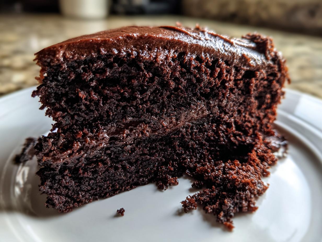 Close-up of a rich, dark slice of chocolate cake with thick, fudgy frosting.