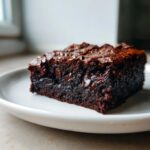 A close-up of a rich, fudgy slice of black bean brownies studded with melted chocolate chips on a white plate.