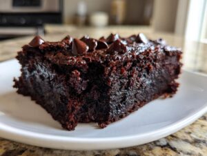 Close-up of a rich, fudgy slice of black bean brownies topped with melted chocolate chips on a white plate.