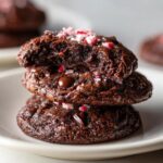A stack of three fudgy chocolate peppermint cookies topped with crushed candy canes.