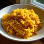 A close-up of vibrant, fluffy turmeric rice seasoned with garlic, served in a white bowl.