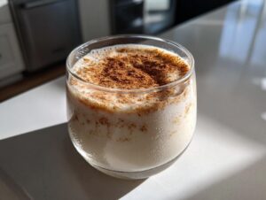 A glass of creamy, chilled coquito topped generously with ground cinnamon spice.