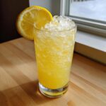 A tall glass filled with bright yellow, icy lemonade, garnished with a lemon wheel.