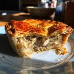 A cross-section of a golden-brown turkey pot pie showing creamy filling with shredded turkey and vegetables.