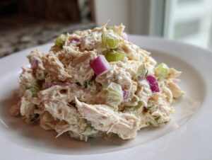 A mound of creamy cottage cheese chicken salad featuring shredded chicken, chunks of red onion, and celery on a white plate.