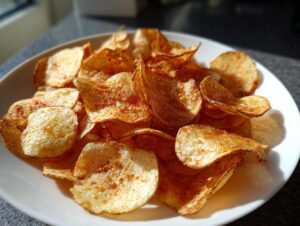 A close-up of a white bowl filled with golden, crispy homemade potato chips seasoned with paprika.