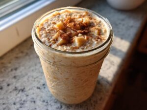 Close-up of apple cinnamon overnight oats in a glass jar, topped with diced apples and cinnamon.