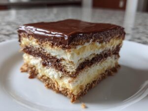 Close-up of a layered slice of eclair cake featuring graham crackers, vanilla pudding, chocolate cream, and chocolate glaze.