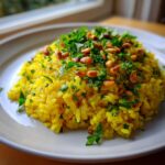 A mound of vibrant yellow mediterranean rice topped with toasted pine nuts and fresh chopped parsley.
