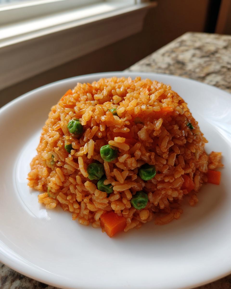 A mound of vibrant orange Mexican rice mixed with bright green peas and diced carrots served on a white plate.