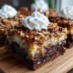 Close-up of a moist german chocolate poke cake square topped with coconut-pecan frosting and whipped cream.