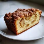 Close-up of a moist slice of jewish apple cake featuring visible apple chunks and a cinnamon sugar crumb topping.