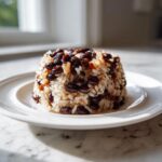 A perfectly molded serving of flavorful black beans and rice on a white plate, bathed in natural light.