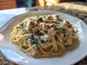 A close-up of a serving of creamy Monterey Chicken Spaghetti topped with chunks of chicken and spinach.