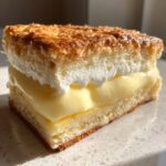 Close-up of a layered slice of bee sting cake showing sponge, custard, cream, and caramelized topping.