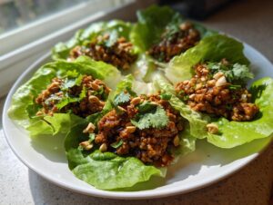 Four servings of thai chicken lettuce wraps on a white plate, topped with chopped peanuts and fresh cilantro.