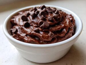 Close-up of rich, dark chocolate brownie batter dip topped generously with mini chocolate chips in a small white bowl.