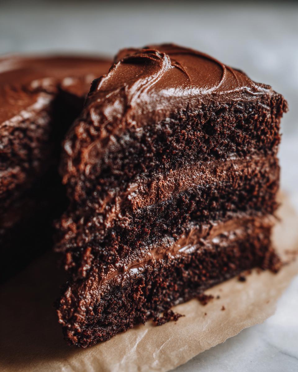 Close-up of a decadent slice of moist chocolate cake layered with dark chocolate frosting.