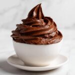 A perfect swirl of rich, dark chocolate frosting piped high in a small white bowl.
