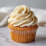 A close-up of a single, perfectly baked vanilla cupcake topped with a swirl of pale yellow vanilla frosting.