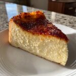 A perfect slice of creamy creme brulee cheesecake featuring a dark, caramelized, torched sugar topping.