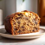 A close-up of a moist slice of date nut bread, rich with visible dates and nuts, on a small plate.