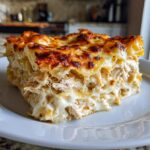 A close-up of a thick, cheesy slice of white sauce chicken lasagna with a golden-brown, bubbly top.