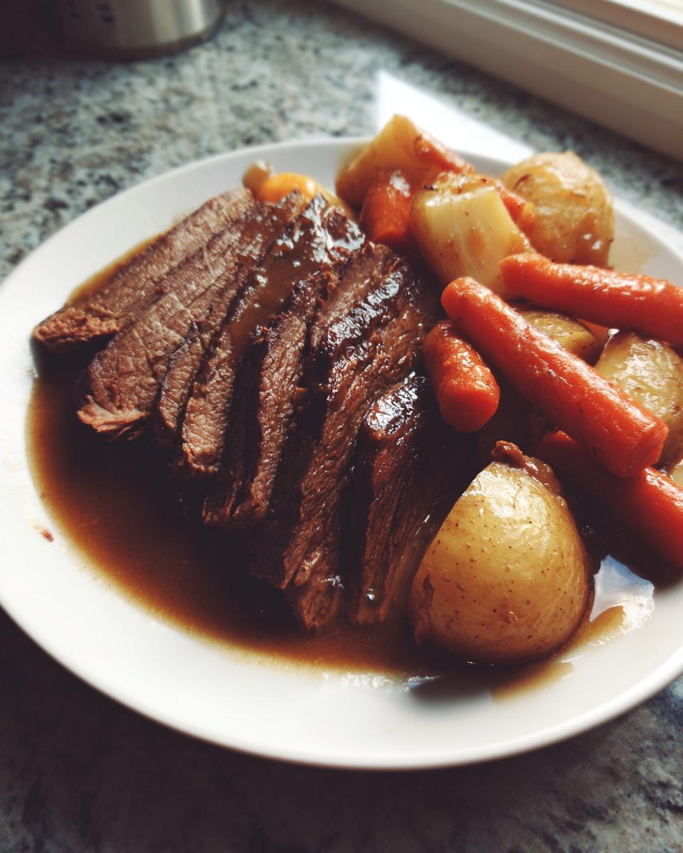 A plate featuring several slices of tender pot roast covered in rich gravy, served alongside carrots and whole potatoes.