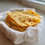 A warm stack of freshly made soft corn tortillas wrapped in a white cloth.