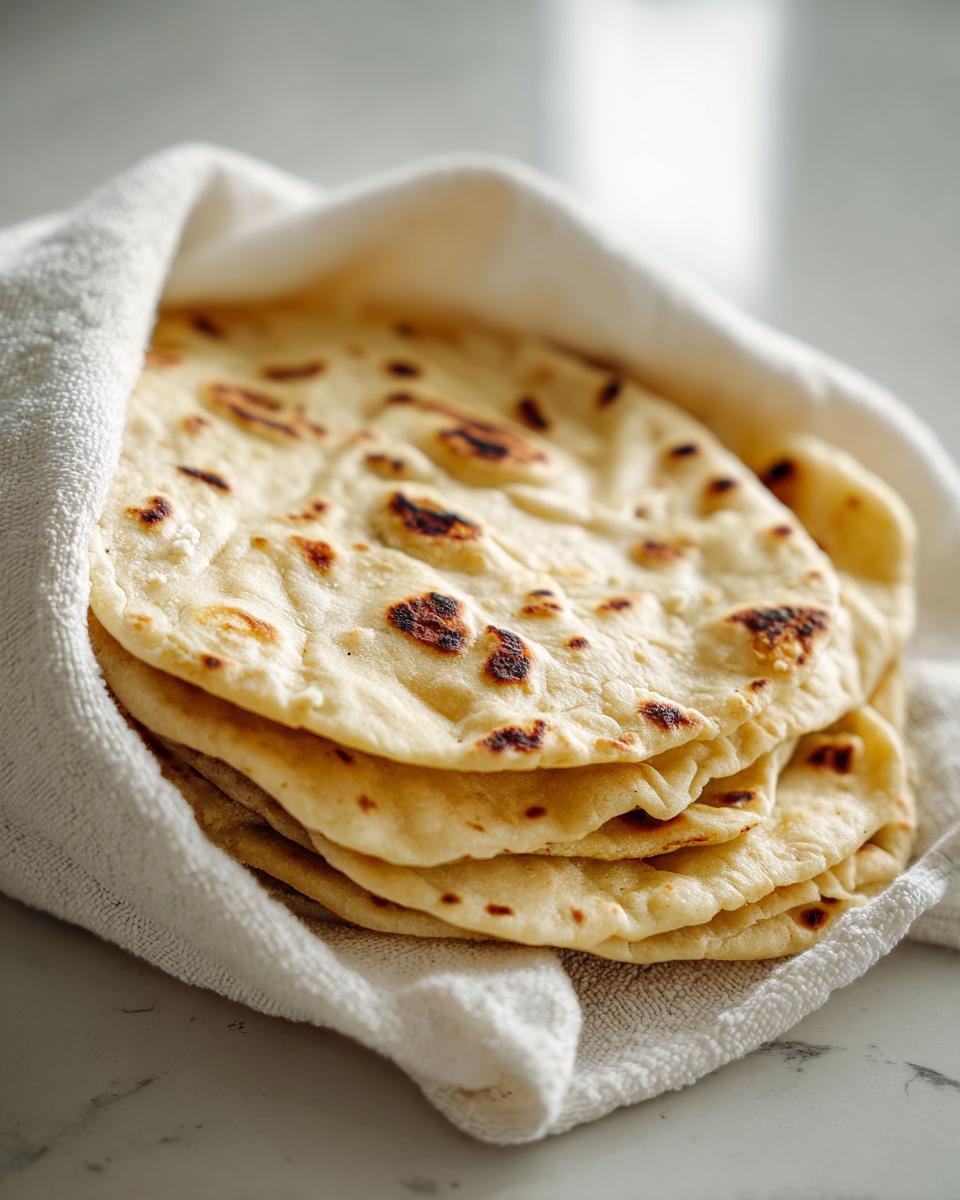 A stack of freshly made, soft corn tortillas wrapped in a white towel to stay warm.