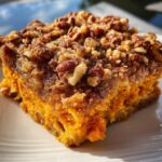 Close-up of a square slice of rich, orange southern sweet potato casserole topped with crunchy pecans and brown sugar crumble.