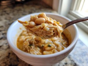 A spoonful of creamy white bean and shredded chicken chili being lifted from a white bowl.