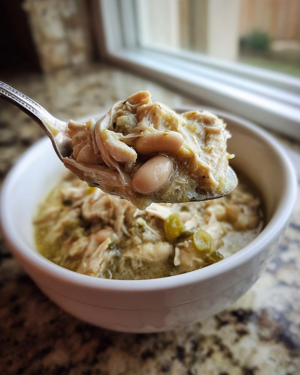 Close-up of a spoonful of creamy white chicken chili, showing shredded chicken and white beans, lifted from a bowl.