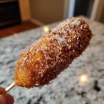 Close-up of a freshly fried korean corn dog generously coated in cinnamon sugar.