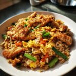 A close-up of a bowl of flavorful chicken fried rice mixed with scrambled egg, carrots, and green onions.