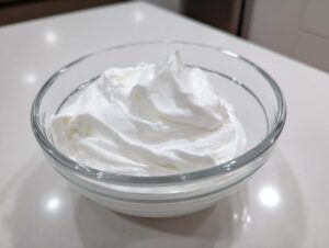 A clear glass bowl filled with thick, glossy white cookie icing, ready for decorating.