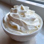 Close-up of thick, bright white royal icing recipe mixture swirled high in a small white bowl.