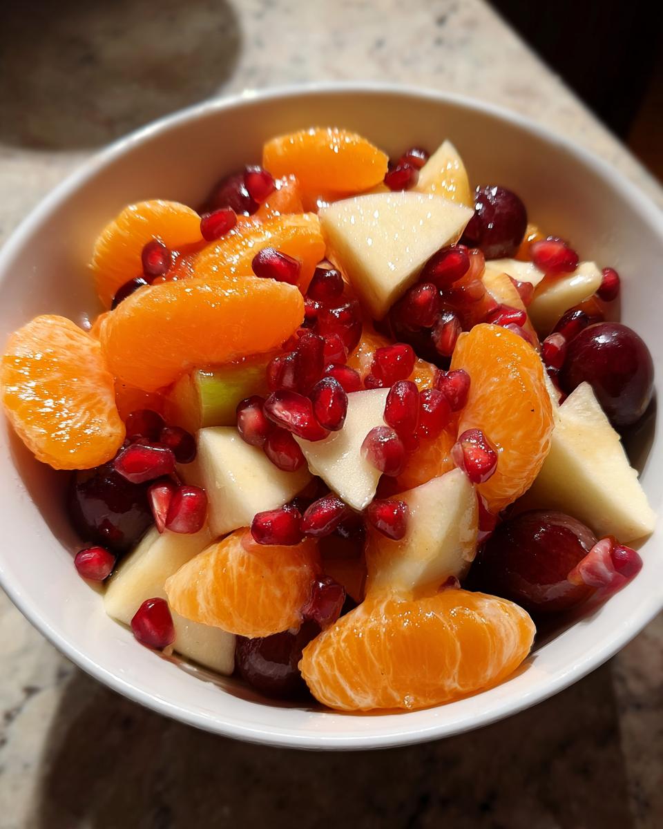 Close-up of a colorful winter fruit salad featuring mandarin segments, apple chunks, grapes, and pomegranate seeds.